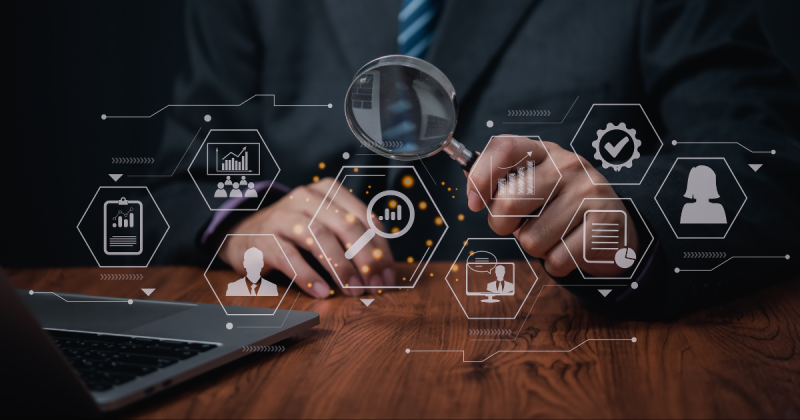 Professional in black suit holds a magnifying glass. Positioned in front of him are graphics showcasing the talent search process.
