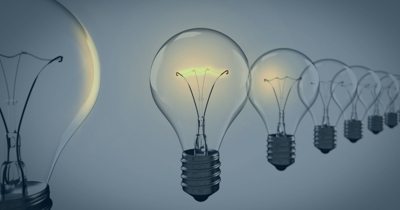 Transparent lightbulbs in a row, with the right bulbs turned on and glowing against a blue-gray background